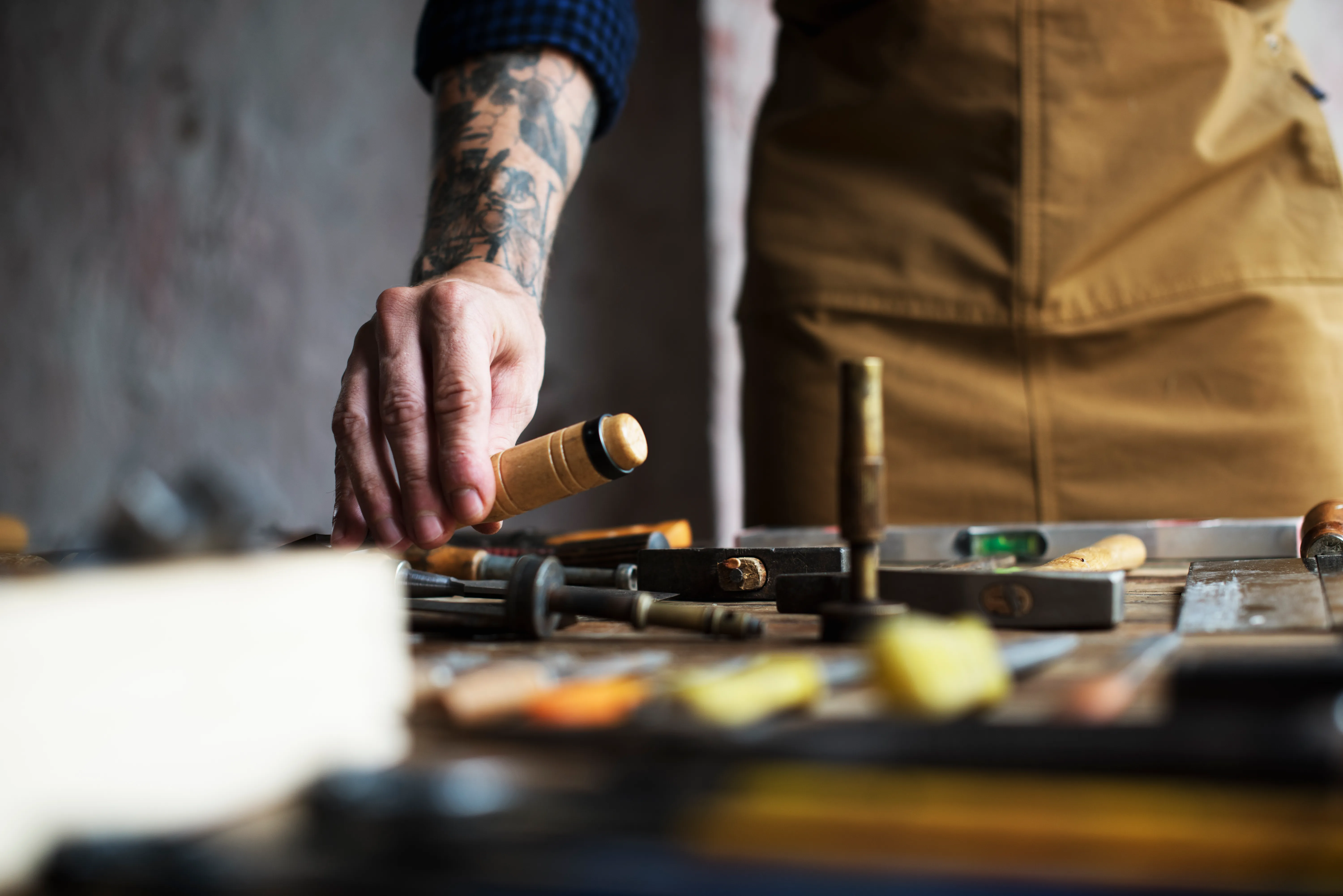 A craftsman's hands reaching for a tool at a workbench.