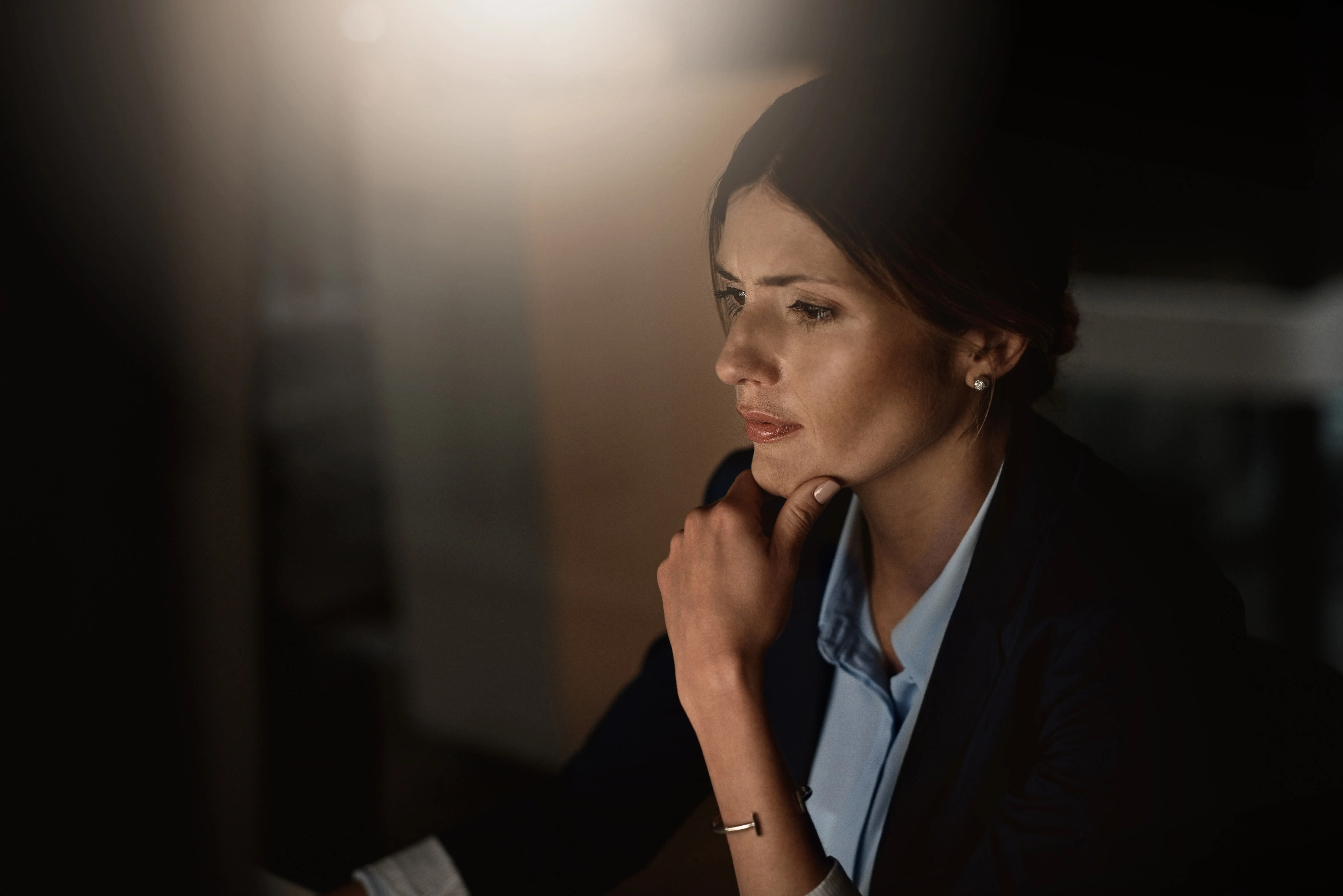 A professional deep in thought at her screen, lit by a single lamp.